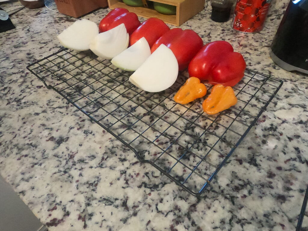 Quartered onions, tomatoes, and peppers lined up on a wire rack ready for the smoker