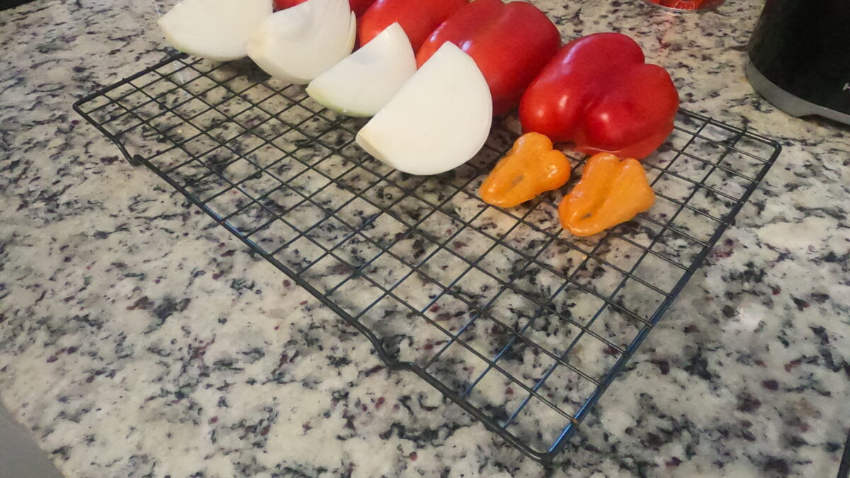 Quartered onions, tomatoes, and peppers lined up on a wire rack ready for the smoker