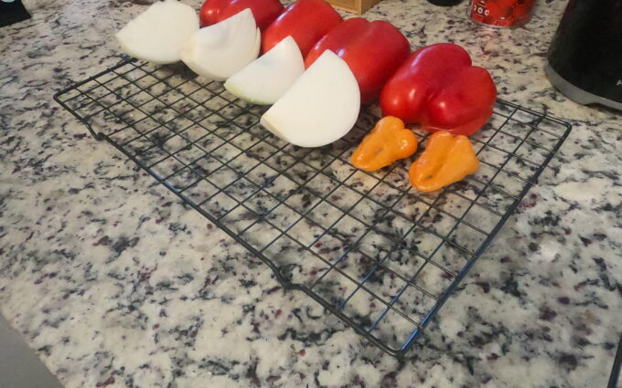 Quartered onions, tomatoes, and peppers lined up on a wire rack ready for the smoker