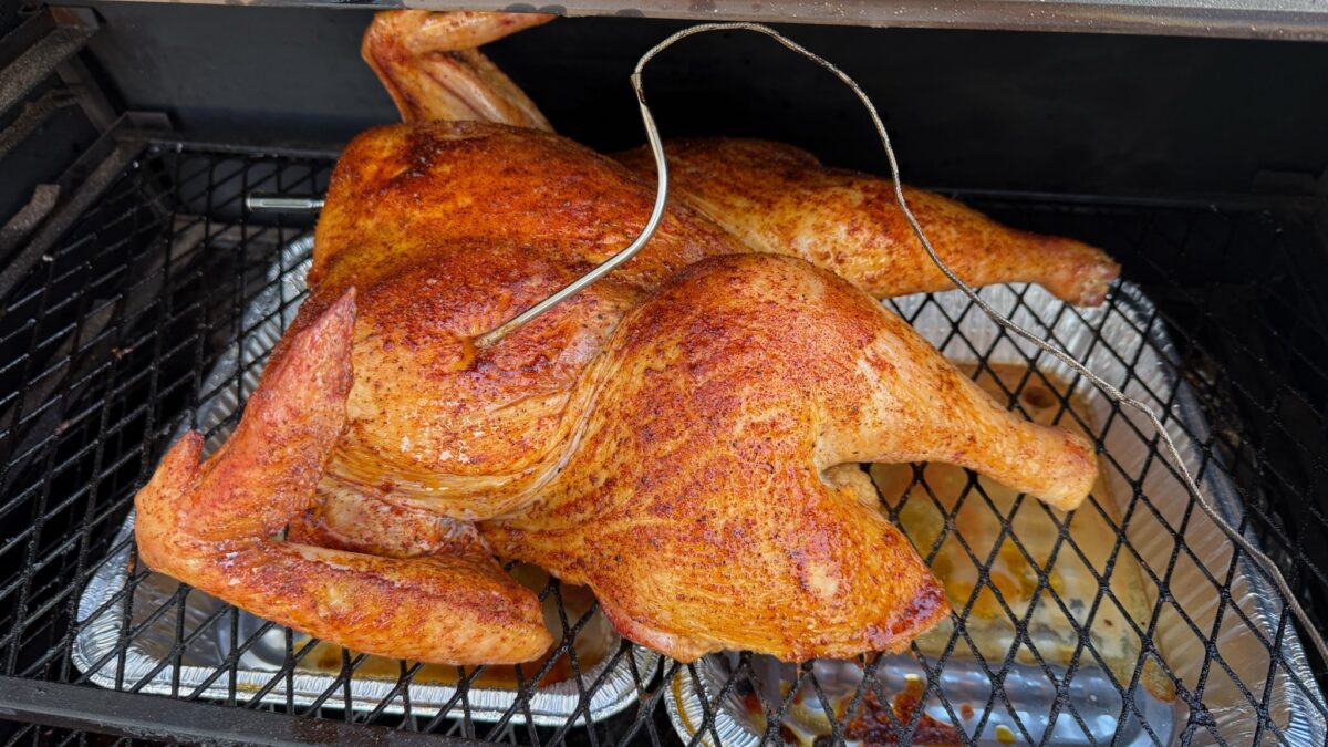 Spatchcocked turkey with deep golden skin on the smoker with a probe thermometer