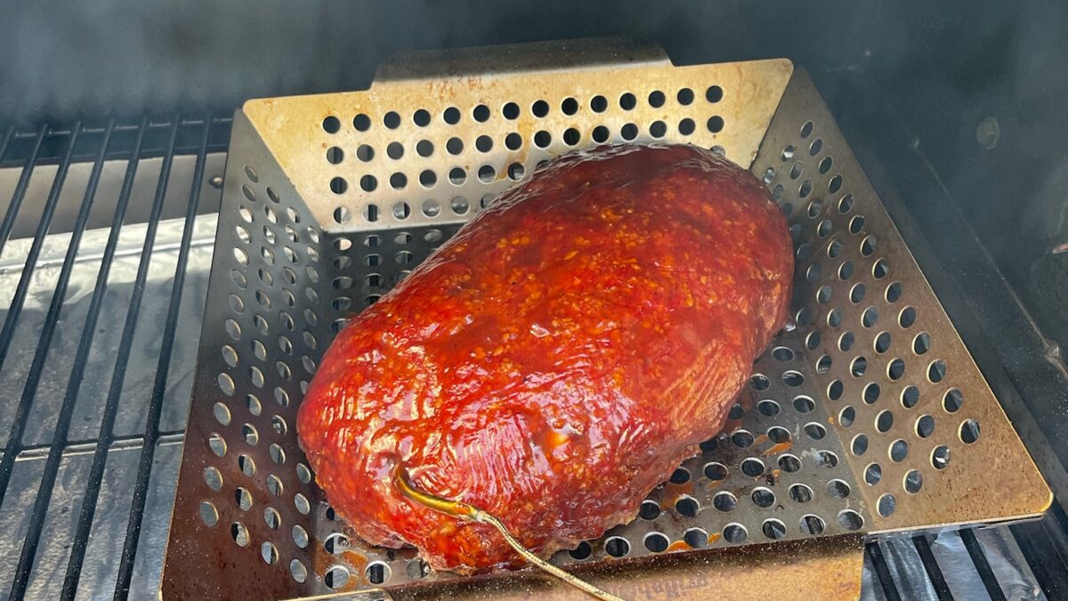 Smoked meatloaf with a deep red glaze on the smoker grates