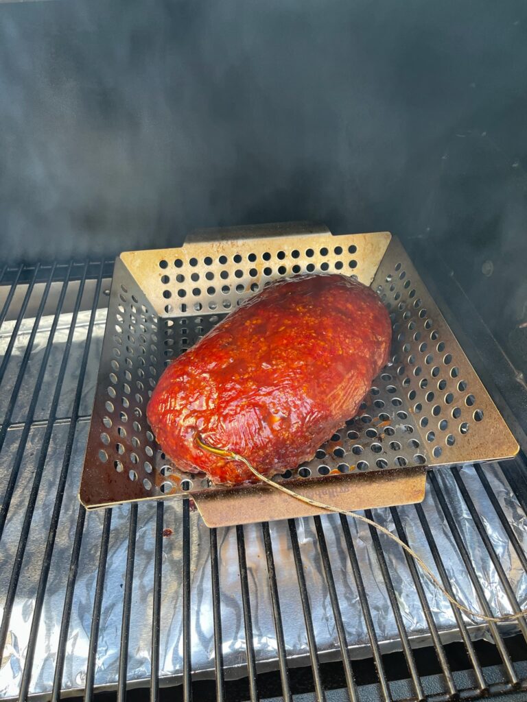 Smoked meatloaf with a deep red glaze on the smoker grates