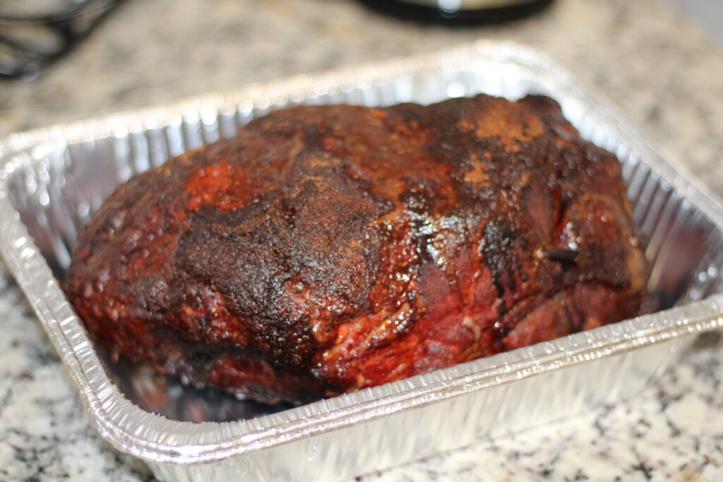 Smoked pork butt with a deep dark bark resting in a foil pan