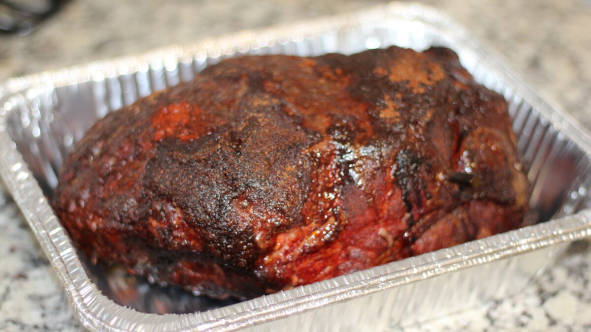 Smoked pork butt with a deep dark bark resting in a foil pan
